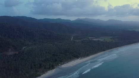 Aerial-view-of-very-long-empty-beach-with-calm-waves-and-palm-trees-at-dusk-on-Long-Beach,-Palawan,-the-Philippines-camera-tracking-pedestal-down
