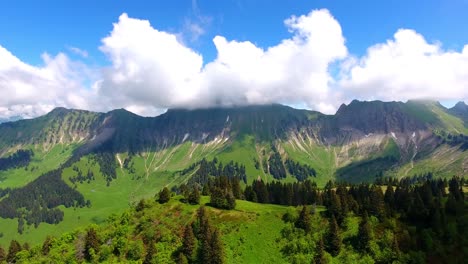 Aerial-shot-over-Alpine-landscape,-Switzerland-in-spring-Forest-and-Alpages,-summits-in-the-background-in-the-clouds