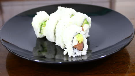 This-is-a-video-of-sushi-on-a-black-plate-with-a-hand-and-chop-sticks-picking-up-a-piece