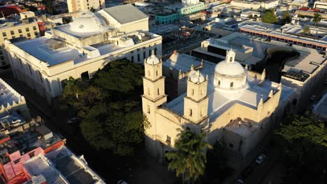 Aerial-camera-at-sunset-slipping-to-the-right-and-rising-behind-the-bell-towers-of-Rectory-Jesus-in-Merida,-Yucatan,-Mexico