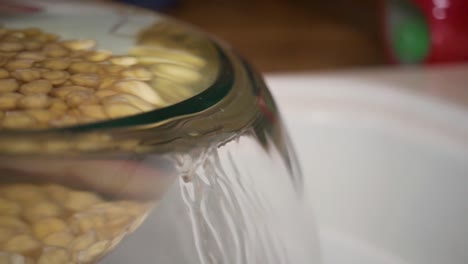 Pouring-water-out-of-glass-bowl-with-chickpeas,-Slow-Motion-Close-Up
