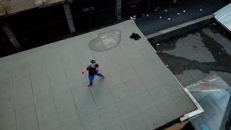 Overhead-Aerial-Drone-Shot-of-a-Young-Adult-Male-Parkour-Free-Runner-Practicing-on-an-Abandoned-Roof-Top