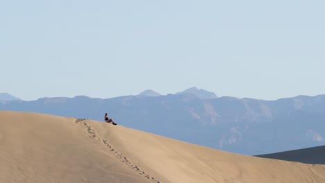 Young-woman-sitting-on-top-of-sand-dune-in-Death-Valley-National-Park-in-California,-USA---slow-motion