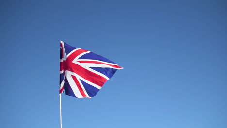 Flag-of-the-United-Kingdom-waving-in-slow-motion-with-clear-blue-sky-in-the-background