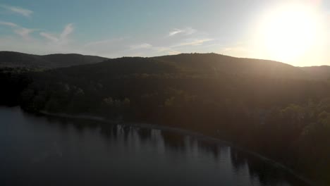 Slow-aerial-flight-over-a-canadian-lake-in-quebec-which-is-surrounded-by-trees-at-sunrise-with-the-sun-shining-over-the-hill-and-trees