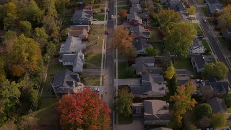 Flyover-suburban-homes-and-autumn-leaves-as-a-white-car-drives-down-the-street-and-out-of-frame