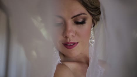 Bride-under-her-veil-ready-for-her-wedding-day-looks-into-camera-and-smile