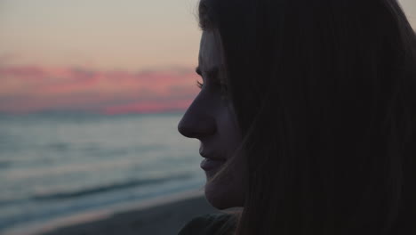 Close-up-of-a-girl-standing-on-the-beach,-looking-into-the-ocean-on-the-sunset-and-thinking-about-memories