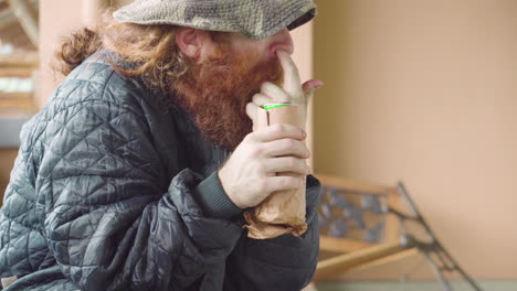 Homeless-Man-outdoors-near-broken-bench-picking-his-nose-with-beer-can-in-hands