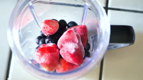 Pouring-frozen-blueberries-and-strawberries-into-blender-to-make-smoothie-or-fitness-shake