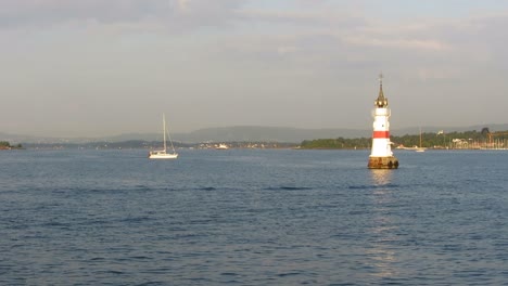 View-from-moving-boat,-passing-lighthouse-and-sailboat