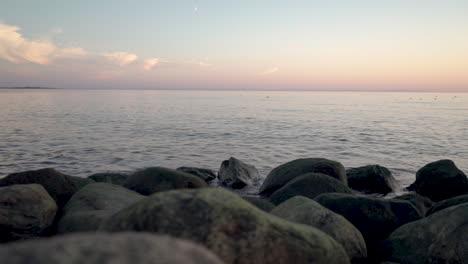 A-panning-wide-shot-from-a-rocky-shore-over-the-sea-during-sunset-in-slowmo