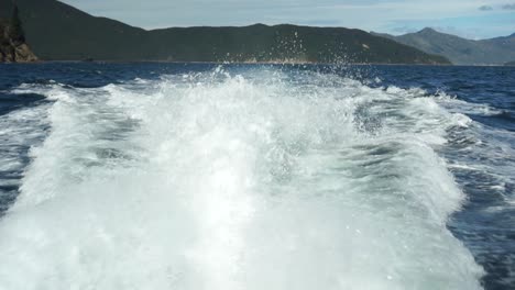 SLOWMO---Back-of-the-boat-waves-with-blue-sky-and-mountains-in-background
