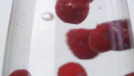 Slow-motion-bright-red-raspberries-splashing-into-cold-glass-of-water-up-close