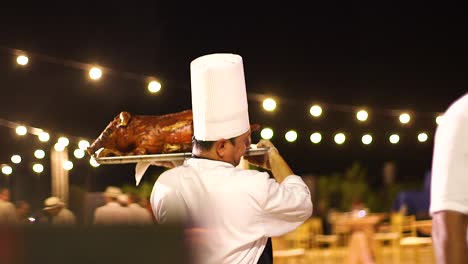 Chef-carrying-a-juicy-cooked-pig-through-an-outdoor-party-at-night-in-Curacao,-Caribbean