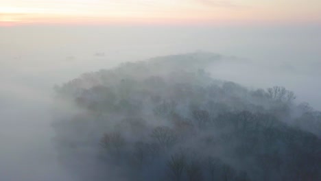 Aerial-view-of-a-forest-near-the-river,-during-sunset,-with-heavy-fog