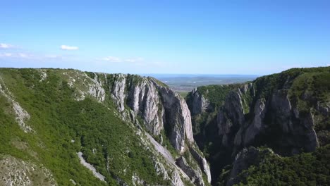 View-from-the-top-of-Cheile-Turzii,-Turda-Gorge,-as-drone-pans-right-revealing-the-landscape-and-the-horizon-beyond-the-ravine
