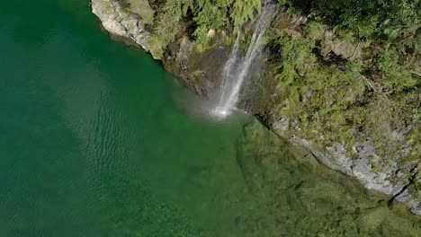 Beautiful-waterfall-on-beautiful-pristine-blue-clear-Pelorus-river,-New-Zealand-with-rocks-and-native-lush-forrest-in-background---Aerial-Drone