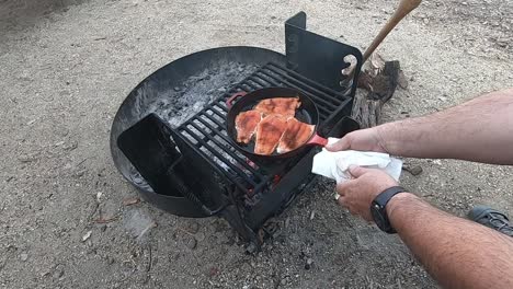 Ensuring-doneness-of-the-cooking-red-salmon-in-a-red-cast-iron-skillet-over-a-campfire