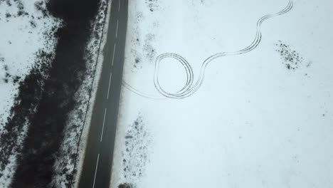 A-car-driving-past-mysterious-tire-tracks-in-snow,-chilly-winter-landscape,-drone-footage,-eerie-feeling-scene