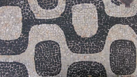 Slow-motion-sideways-moving-top-down-closeup-view-of-the-so-called-Portuguese-pavement-design-in-Ipanema,-Rio-de-Janeiro,-with-typical-shapes-on-the-beach-boulevard-sidewalk