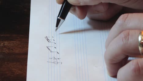 Composer-writing-music-notes-on-sheet-with-pen-hand-close-up