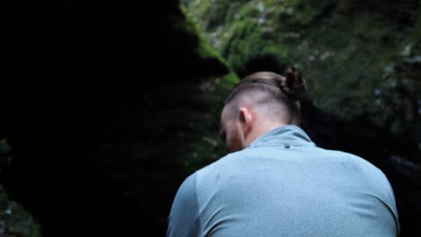 Back-view-of-young-man-slowly-walking-further-into-a-shadowy-ravine