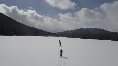 Drone-shot-of-backcountry-skiers-skinning-across-frozen-lake-in-winter