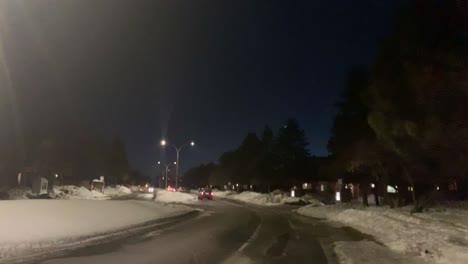View-from-the-sidewalk-of-a-car-going-down-a-curvy-town-road-at-night-in-the-winter