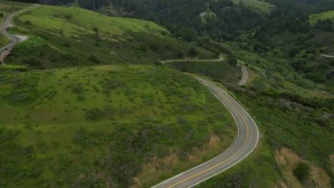 Aerial-pull-back-shot-of-a-very-windy-section-of-highway-1-in-northern-California-with-cars-driving-past