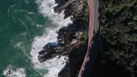 Aerial-top-down-following-the-coastline-Niemeyer-avenue-with-a-broad-bicycle-path-aside-the-waves-crashing-on-the-rock-beach
