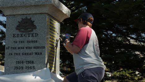 Female-restoration-artist-repairs-the-painted-lettering-on-a-world-war-memorial