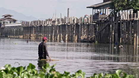 Männlicher-Burmesischer-Fischer,-Der-Durch-Einen-See-In-Der-Nähe-Einer-Brücke-In-Myanmar-Geht