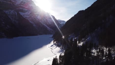 Luftaufnahme-über-Ein-Wunderschönes-Tal-Mit-Einem-Zugefrorenen-See-Und-Zwei-Großen-Schneebedeckten-Bergen-Im-Klöntal-In-Der-Schweiz