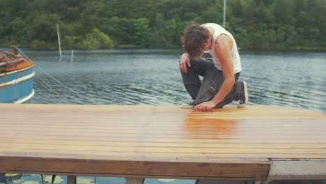 Youth-walks-into-frame-to-start-hand-sanding-roof-of-wooden-boat-planking