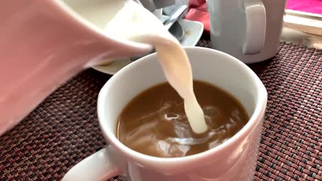 In-Zeitlupe-Wird-Frische-Weiße-Milch-In-Eine-Tasse-Kaffee-Gegossen