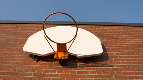 Looking-up-at-a-basketball-hoop-on-the-brick-wall-of-a-schoolyard-on-a-sunny-morning