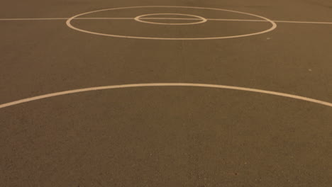 Pan-up-to-reveal-an-empty,-outdoor-basketball-court-in-the-early-morning-sun