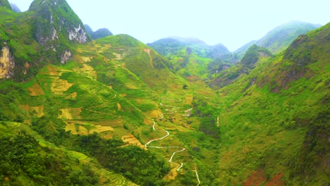 Aerial-dolly-forward-of-a-winding-road-cut-into-the-mountainside-of-the-misty-mountains-of-Ma-Pi-Leng-Pass-in-northern-Vietnam