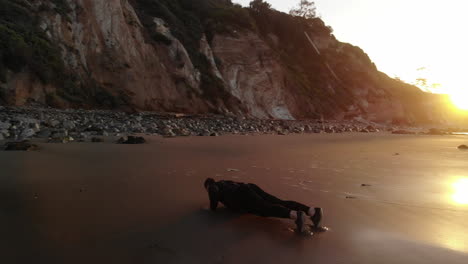 A-strong-muscular-man-doing-push-ups-for-a-morning-fitness-workout-at-sunrise-on-a-beach-in-Santa-Barbara,-California