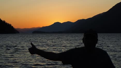 Sunset-on-a-lake-with-mountains-in-the-background-and-man-walking-giving-the-thumbs-up