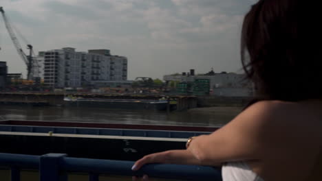 Slow-Motion-of-a-Beautiful-latina-woman-on-holiday-leaning-against-the-railing,-looking-at-the-river-Thames-in-London,-looking-at-the-camera,-smiling-and-wandering-around