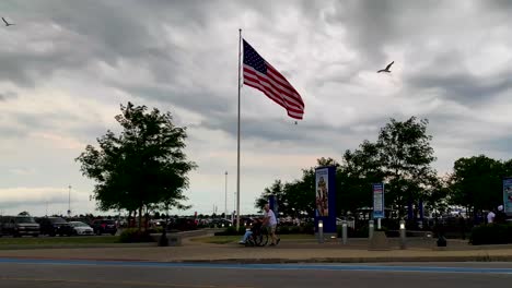 Disabled-young-girl-returning-from-a-cedar-point-amusement-park-after-enjoying-rides-with-a-american-flag-in-the-background-and-clouds