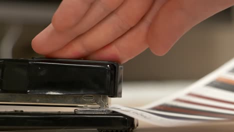 A-close-up-from-the-side-of-a-black-stapler-stapling-pieces-of-paper-together-in-slow-motion