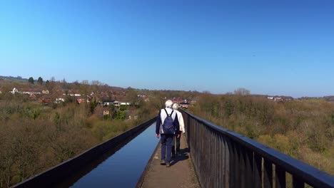 An-elderly-couple-with-grey-hair-walk-across-the-famous-Pontcysyllte-Aqueduct-on-the-Llangollen-canal-route-in-the-beautiful-Welsh-countryside