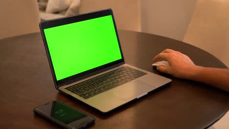 Hombre-Usando-Laptop,-Celular-En-Primer-Plano,-Pantalla-Verde