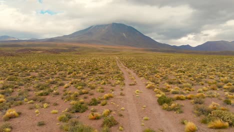 Aerial-action-cinematic-shot-following-a-dirt-road-approaching-a-volcano-in-the-Atacama-Desert,-Chile,-South-America