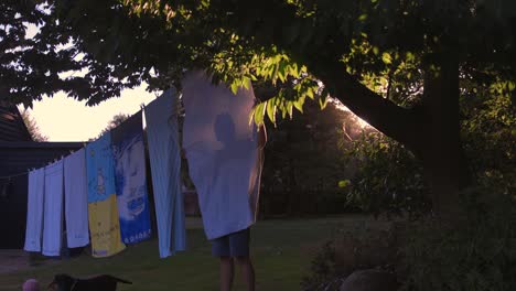 Man-silhouetted-hanging-towels-onto-washing-line-at-sunset