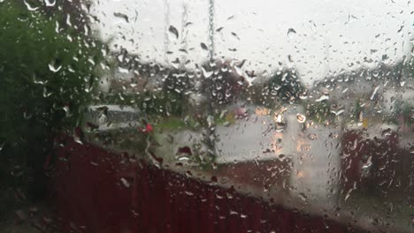 Rain-Falling-On-Window-With-Blurred-Background-Of-Traffic-Outside-Street-Going-Past