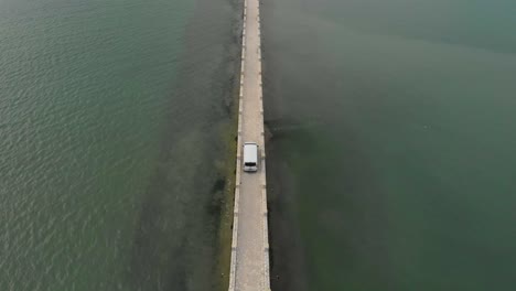 aerial-drone-footage-following-white-van-passes-on-bridge-road-arriving-at-small-greek-exotic-island,-Koukoumitsa-Vonitsa-Greece